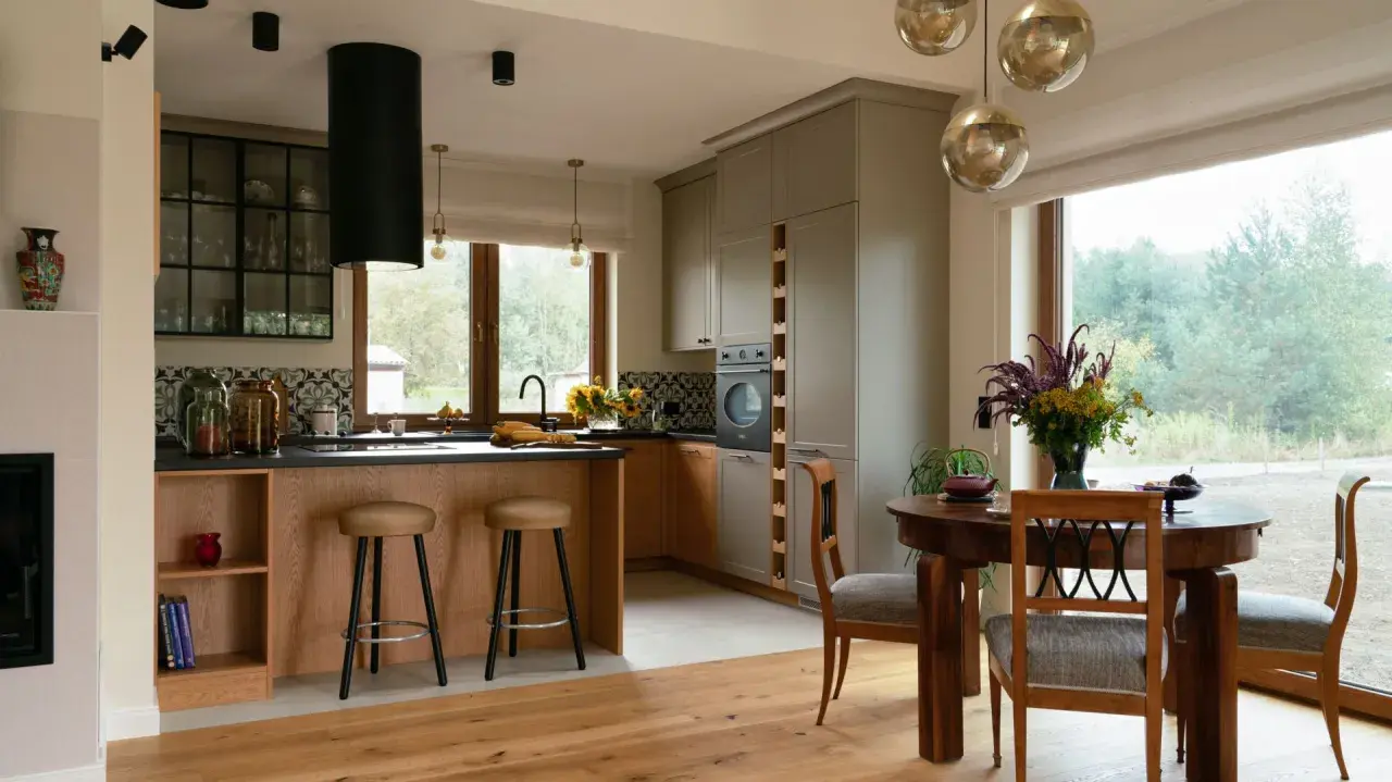 Przytulna kuchnia w stylu modern farmhouse z drewnianą wyspą, szarymi szafkami i dużym oknem z widokiem na zieleń.