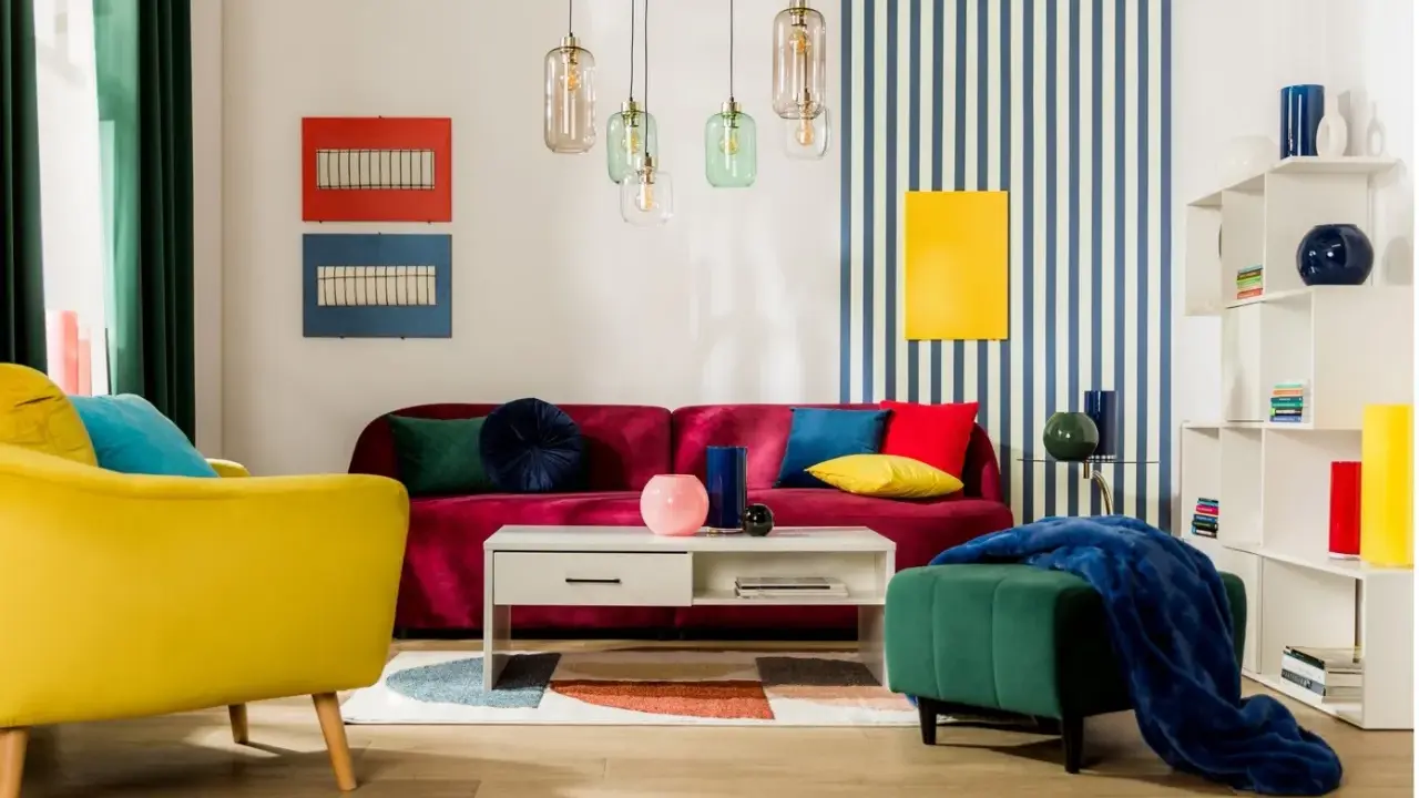 Salon w stylu memphis z kanapą w kolorze fuksji, żółtym fotelem i zieloną pufą. Kolorowe poduszki i geometryczne dekoracje.