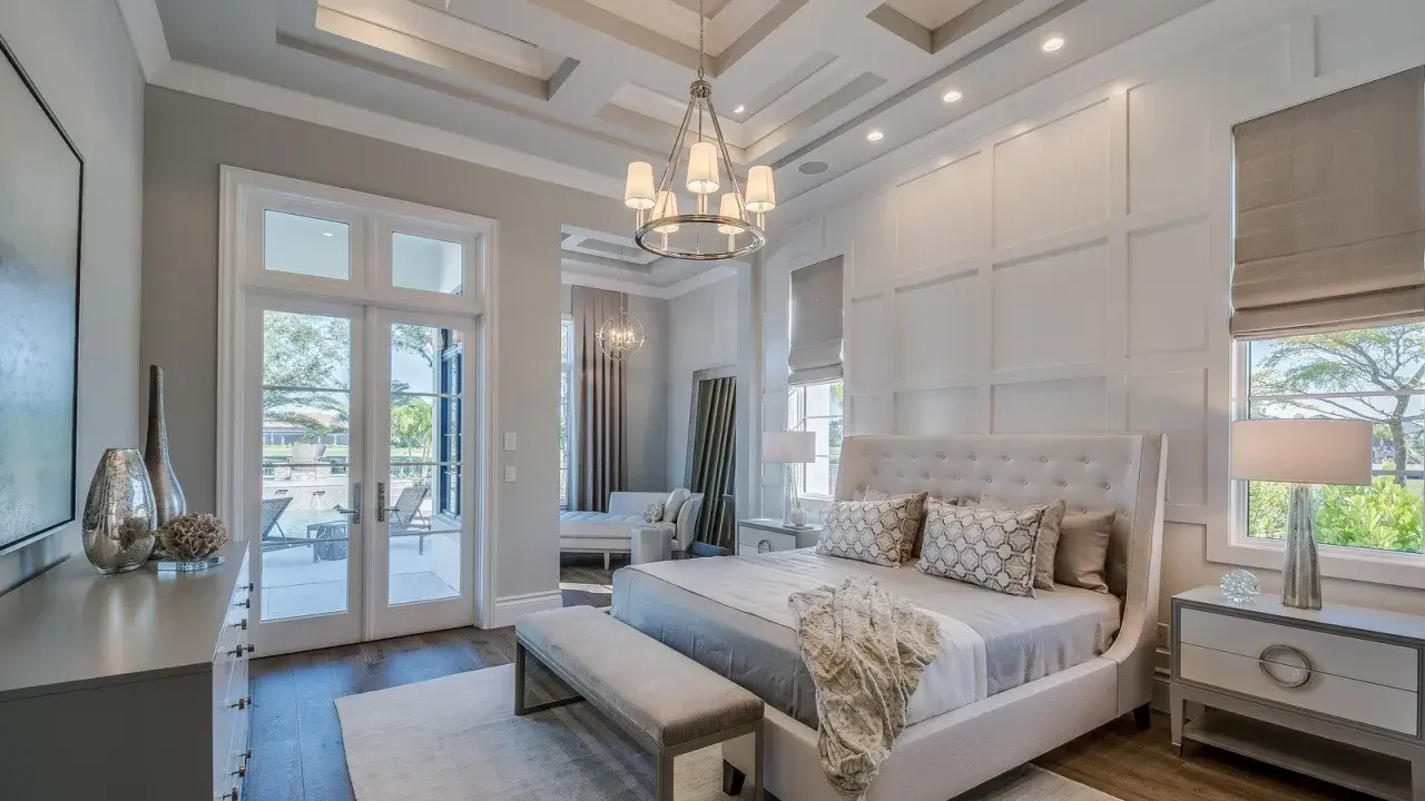 Elegancki master bedroom z łóżkiem z wysokim zagłówkiem, ozdobnymi poduszkami i narzutą. Widok na taras z basenem.