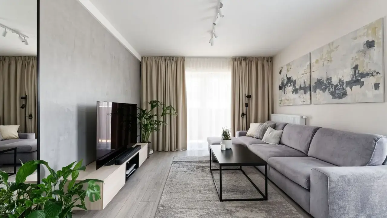 Nowoczesny salon z szarą kanapą i betonową ścianą. Obrazy nad kanapą to świetny pomysł na ścianę za kanapą.