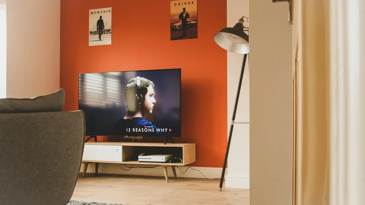 Pomarańczowe ściany świetnie komponują się z szarą kanapą i drewnianymi meblami. Idealne do relaksu i oglądania filmów.