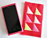 Różowe etui na telefon Nokia obok czerwonego pokrowca z kolorowymi trójkątami. Idealne, by pokazać, jak uszyć etui na telefon.