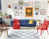 Salon w stylu eklektyzm: granatowa kanapa, czerwony fotel, dywan z geometrycznym wzorem, galeria obrazów na ścianie.