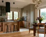 Przytulna kuchnia w stylu modern farmhouse z drewnianą wyspą, szarymi szafkami i dużym oknem z widokiem na zieleń.
