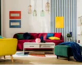 Salon w stylu memphis z kanapą w kolorze fuksji, żółtym fotelem i zieloną pufą. Kolorowe poduszki i geometryczne dekoracje.