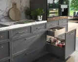 Elegancka organizacja szafek w kuchni. W otwartych szufladach widać garnki i patelnie, a na blacie ekspres do kawy i zioła.