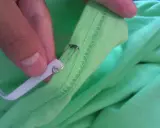 Ręka z agrafką i białą gumką, pokazująca jak skrócić koszulkę bez maszyny.