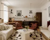Przytulny salon z elementami styl vintage wnętrza: kremowa sofa, fotele w rudy wzór, okrągły stolik i dywan z geometrycznym motywem.