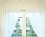 Eleganckie upinanie firan przykłady: białe, zwiewne zasłony tworzą lekki łuk, odsłaniając widok na zieleń i budynki.