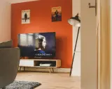Pomarańczowe ściany świetnie komponują się z szarą kanapą i drewnianymi meblami. Idealne do relaksu i oglądania filmów.