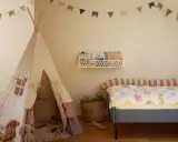 Jasny, neutralny pokój dziecka z namiotem tipi, łóżkiem z kolorową pościelą i girlandą. Jaki kolor do pokoju dziecka? Jasne, pastelowe barwy stworzą przytulną atmosferę.