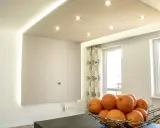 Nowoczesne aranżacje sufitów podwieszanych z subtelnym wzorem i oświetleniem LED. Miska pomarańczy na pierwszym planie.