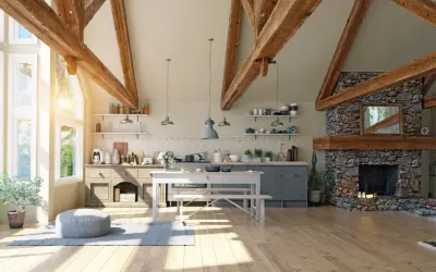 Jasna kuchnia w stylu modern farmhouse z kamiennym kominkiem, drewnianymi belkami i dużymi oknami.