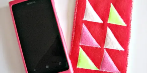 Różowe etui na telefon Nokia obok czerwonego pokrowca z kolorowymi trójkątami. Idealne, by pokazać, jak uszyć etui na telefon.