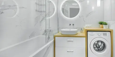Nowoczesne, małe łazienki z wanną, umywalką nablatową i pralką. Marmurowe płytki i okrągłe lustro z podświetleniem tworzą elegancki styl.
