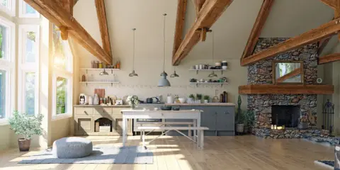 Jasna kuchnia w stylu modern farmhouse z kamiennym kominkiem, drewnianymi belkami i dużymi oknami.
