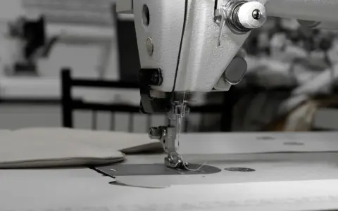 Precyzyjne stebnowanie na maszynie, tworzące idealne szwy na jasnym materiale.