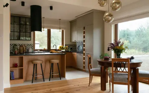 Przytulna kuchnia w stylu modern farmhouse z drewnianą wyspą, szarymi szafkami i dużym oknem z widokiem na zieleń.