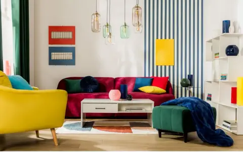 Salon w stylu memphis z kanapą w kolorze fuksji, żółtym fotelem i zieloną pufą. Kolorowe poduszki i geometryczne dekoracje.