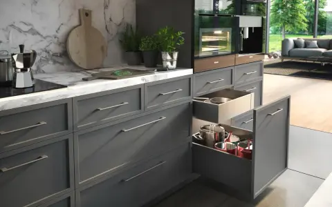 Elegancka organizacja szafek w kuchni. W otwartych szufladach widać garnki i patelnie, a na blacie ekspres do kawy i zioła.