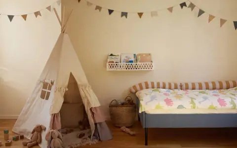 Jasny, neutralny pokój dziecka z namiotem tipi, łóżkiem z kolorową pościelą i girlandą. Jaki kolor do pokoju dziecka? Jasne, pastelowe barwy stworzą przytulną atmosferę.