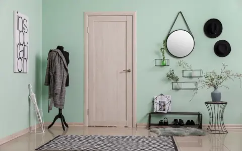 Przedpokój z miętowym kolorem ścian, manekin w płaszczu, lustro, półki z dekoracjami i drzwi.
