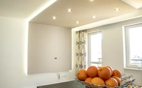 Nowoczesne aranżacje sufitów podwieszanych z subtelnym wzorem i oświetleniem LED. Miska pomarańczy na pierwszym planie.