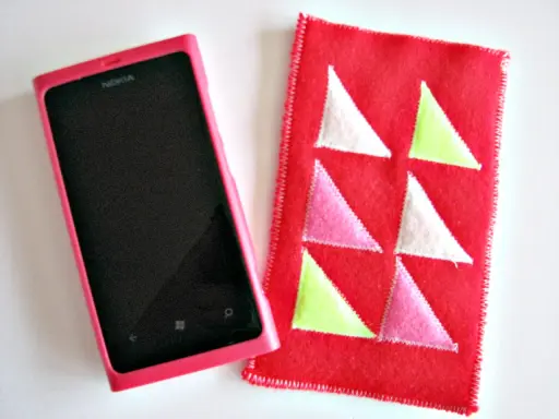 Różowe etui na telefon Nokia obok czerwonego pokrowca z kolorowymi trójkątami. Idealne, by pokazać, jak uszyć etui na telefon.