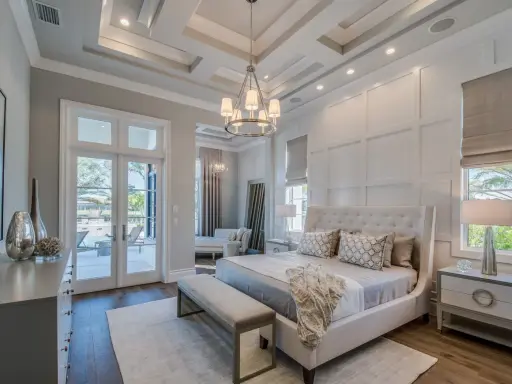 Elegancki master bedroom z łóżkiem z wysokim zagłówkiem, ozdobnymi poduszkami i narzutą. Widok na taras z basenem.