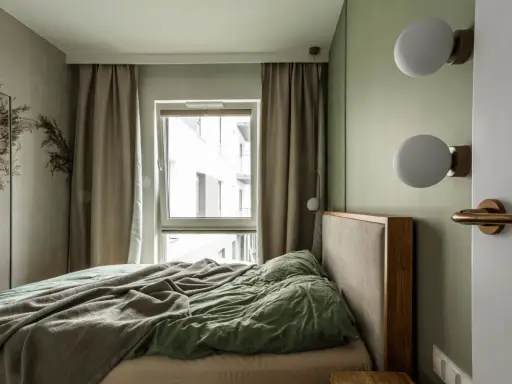 Przytulna, mała sypialnia z dużym łóżkiem, zasłonami i oknem. Dwa kinkiety nad wezgłowiem dodają uroku.