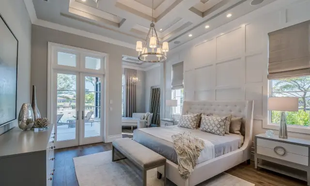 Elegancki master bedroom z łóżkiem z wysokim zagłówkiem, ozdobnymi poduszkami i narzutą. Widok na taras z basenem.
