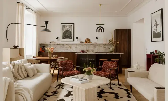 Przytulny salon z elementami styl vintage wnętrza: kremowa sofa, fotele w rudy wzór, okrągły stolik i dywan z geometrycznym motywem.