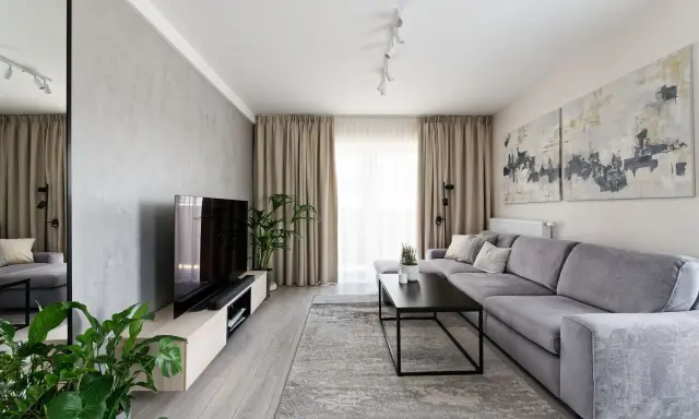 Nowoczesny salon z szarą kanapą i betonową ścianą. Obrazy nad kanapą to świetny pomysł na ścianę za kanapą.