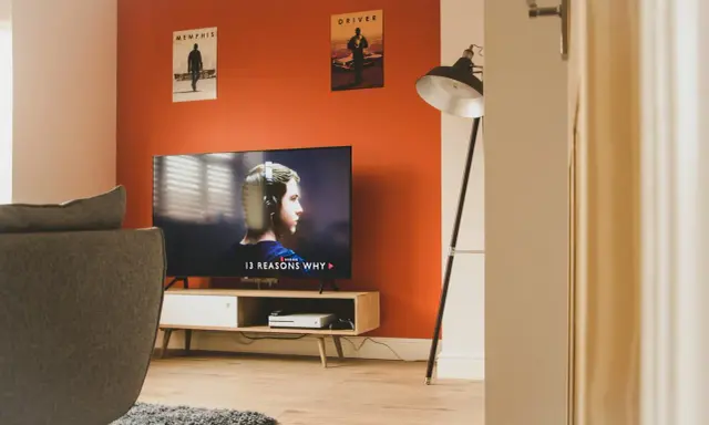 Pomarańczowe ściany świetnie komponują się z szarą kanapą i drewnianymi meblami. Idealne do relaksu i oglądania filmów.