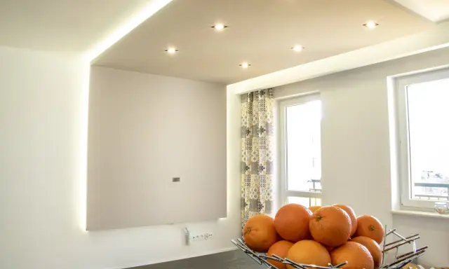 Nowoczesne aranżacje sufitów podwieszanych z subtelnym wzorem i oświetleniem LED. Miska pomarańczy na pierwszym planie.