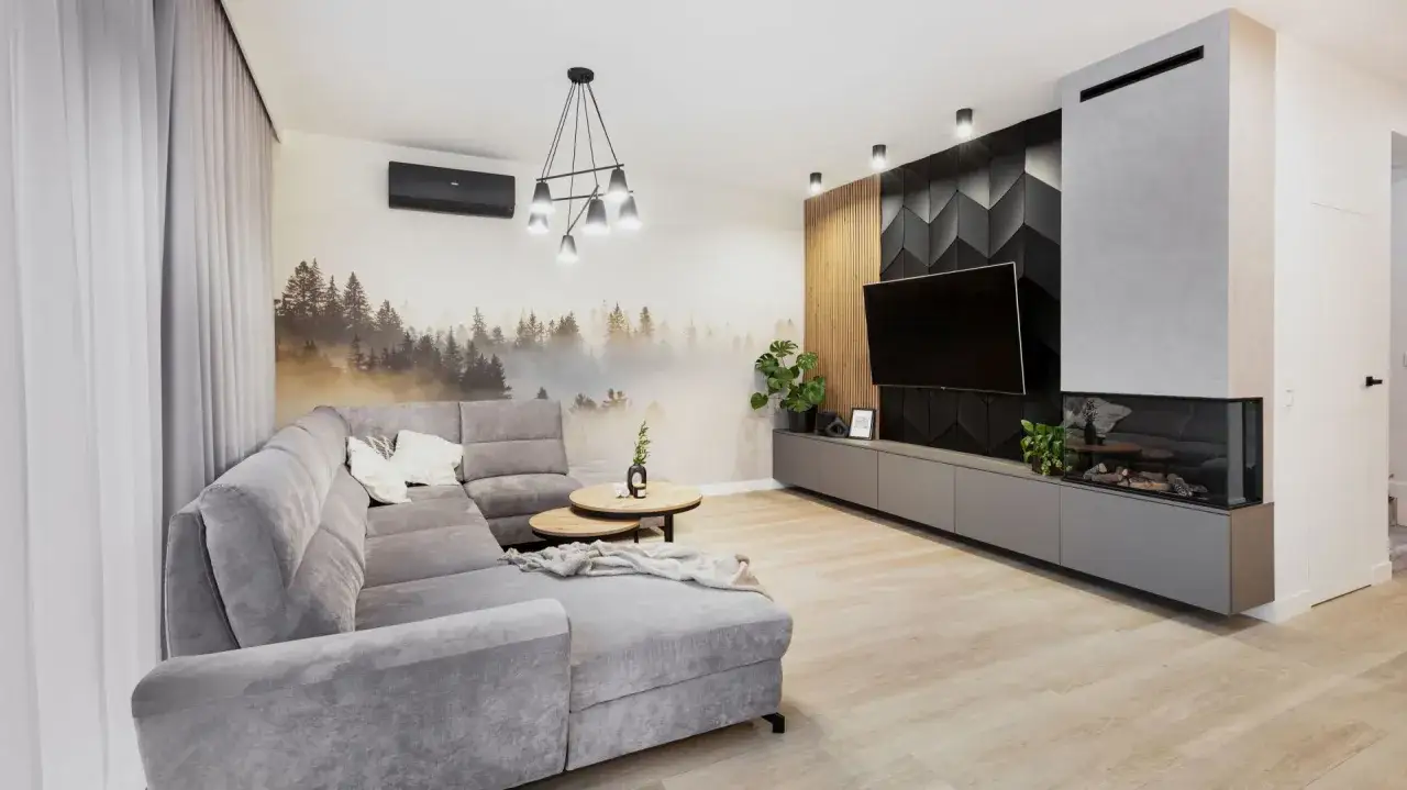 Nowoczesny salon z szarą sofą i fototapetą z lasem. Bardzo jasny szary kolor ścian tworzy przytulną atmosferę.