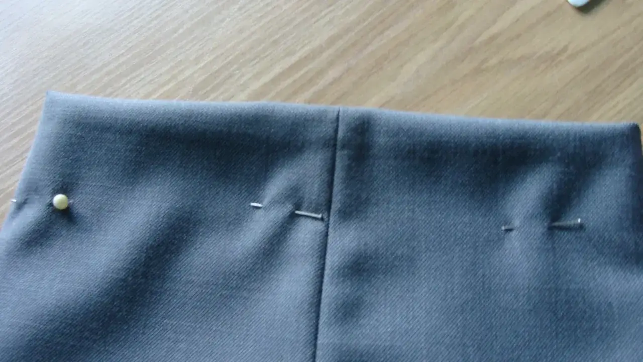 Szare spodnie z widocznymi zaszewkami, przygotowane do szycia. Szpilki trzymają materiał w miejscu.